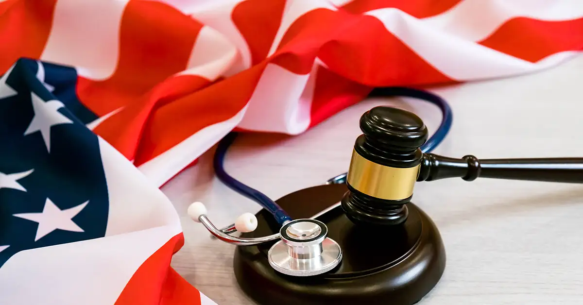 A wooden gavel and a stethoscope placed on a judge’s sound block, with the American flag in the background.